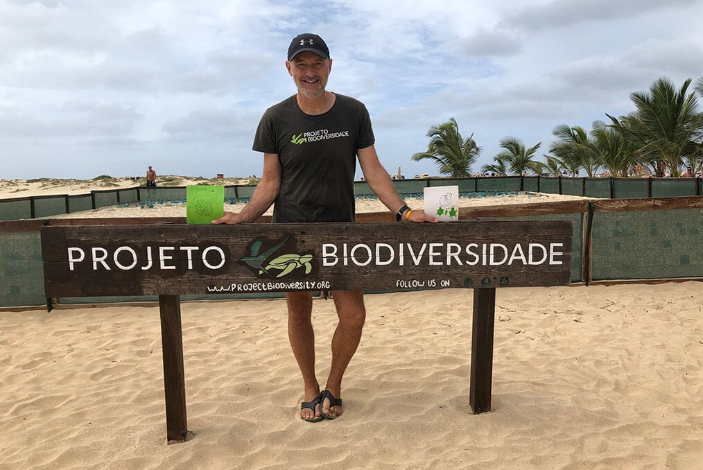 A man standing in front of a sign that reads Projecto Biodiversidade